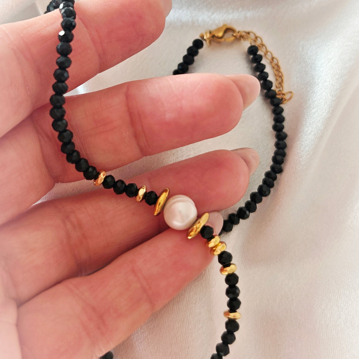Noir Muse black crystal and pearl necklace held in hand, showing gold-tone details and extension chain.