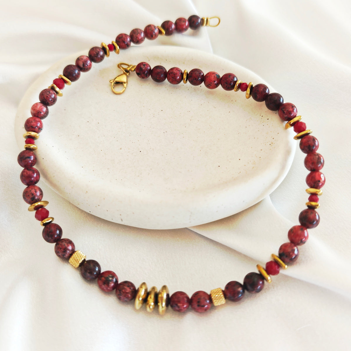 Burgundy Rhythm necklace with round burgundy semiprecious beads and gold-tone details on an ivory display.