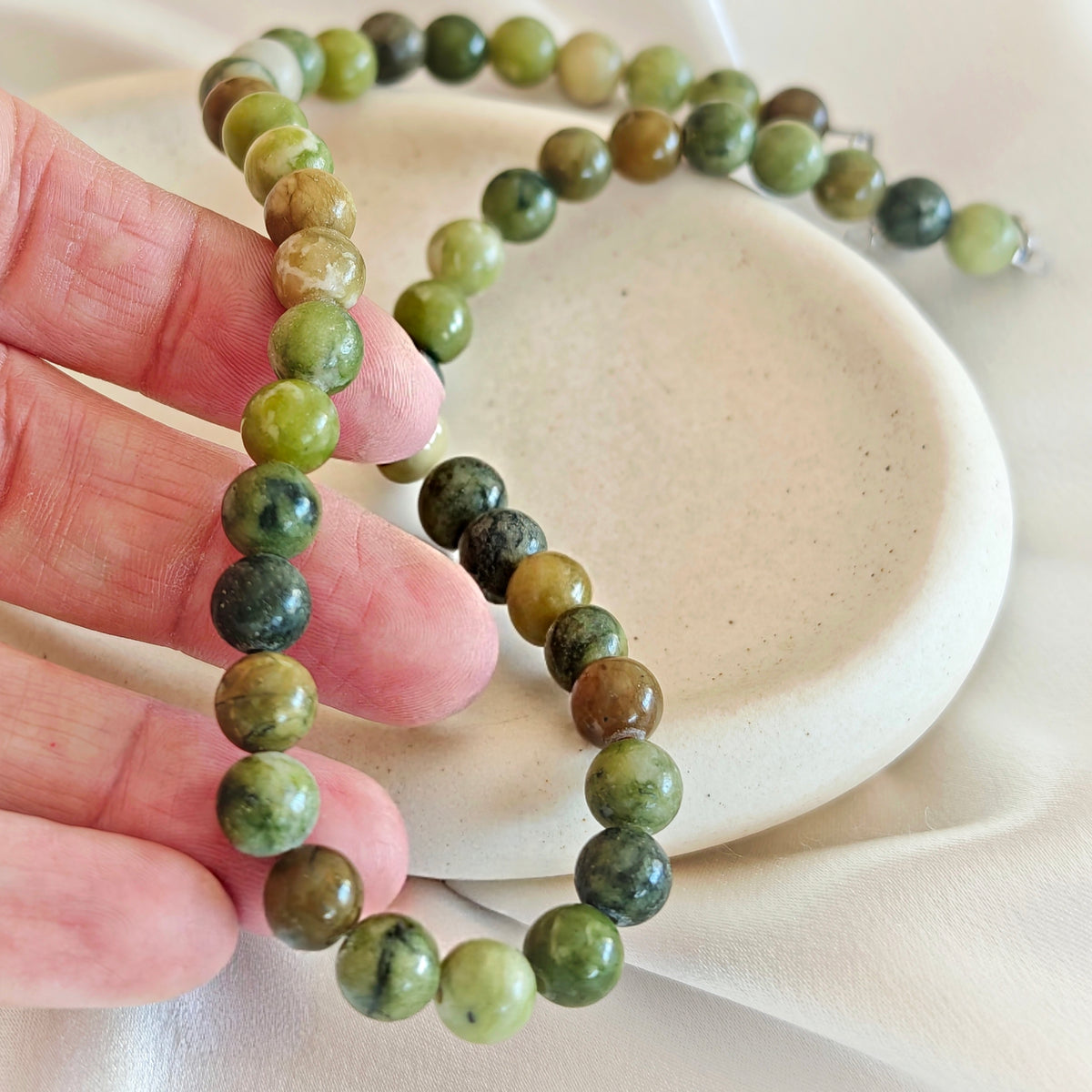 Close-up of round Olive Green agate beads in light and dark green shades held in a hand.