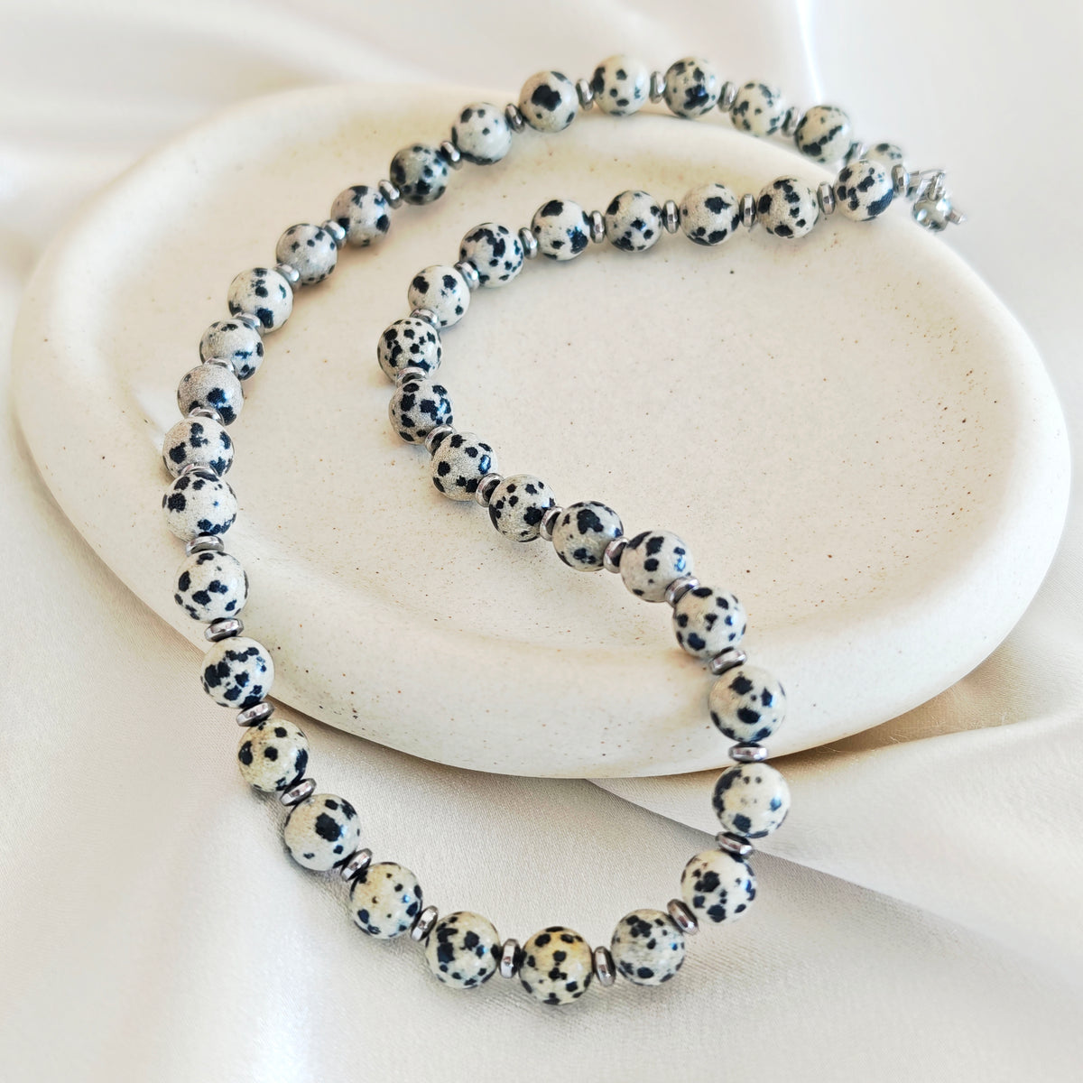Dalmatian jasper necklace with cream beads, black spots and silver-tone hematite details on an ivory display.