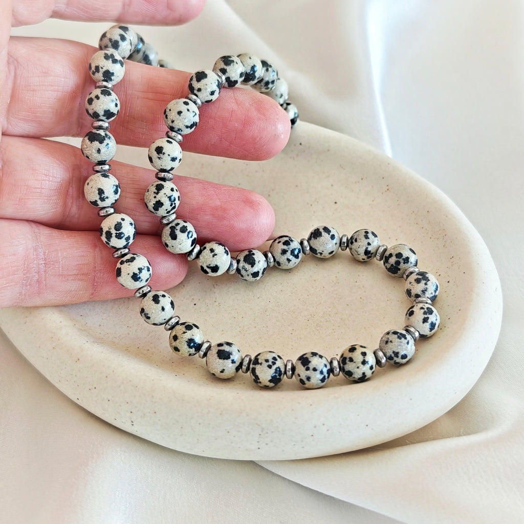 Close-up of Dalmatian jasper beads with black spots and silver-tone details held in a hand.