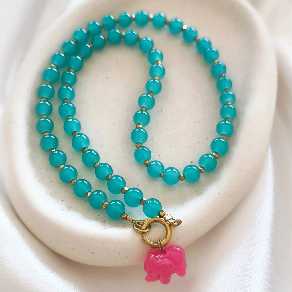 christisaccessories beaded necklace with turquoise beads, gold spacers, and a pink elephant charm on a white dish.