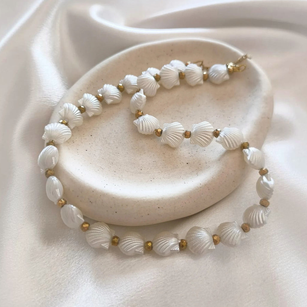 christisaccessories pearlescent white seashell beaded necklace with gold-toned metallic accents on a ceramic dish.