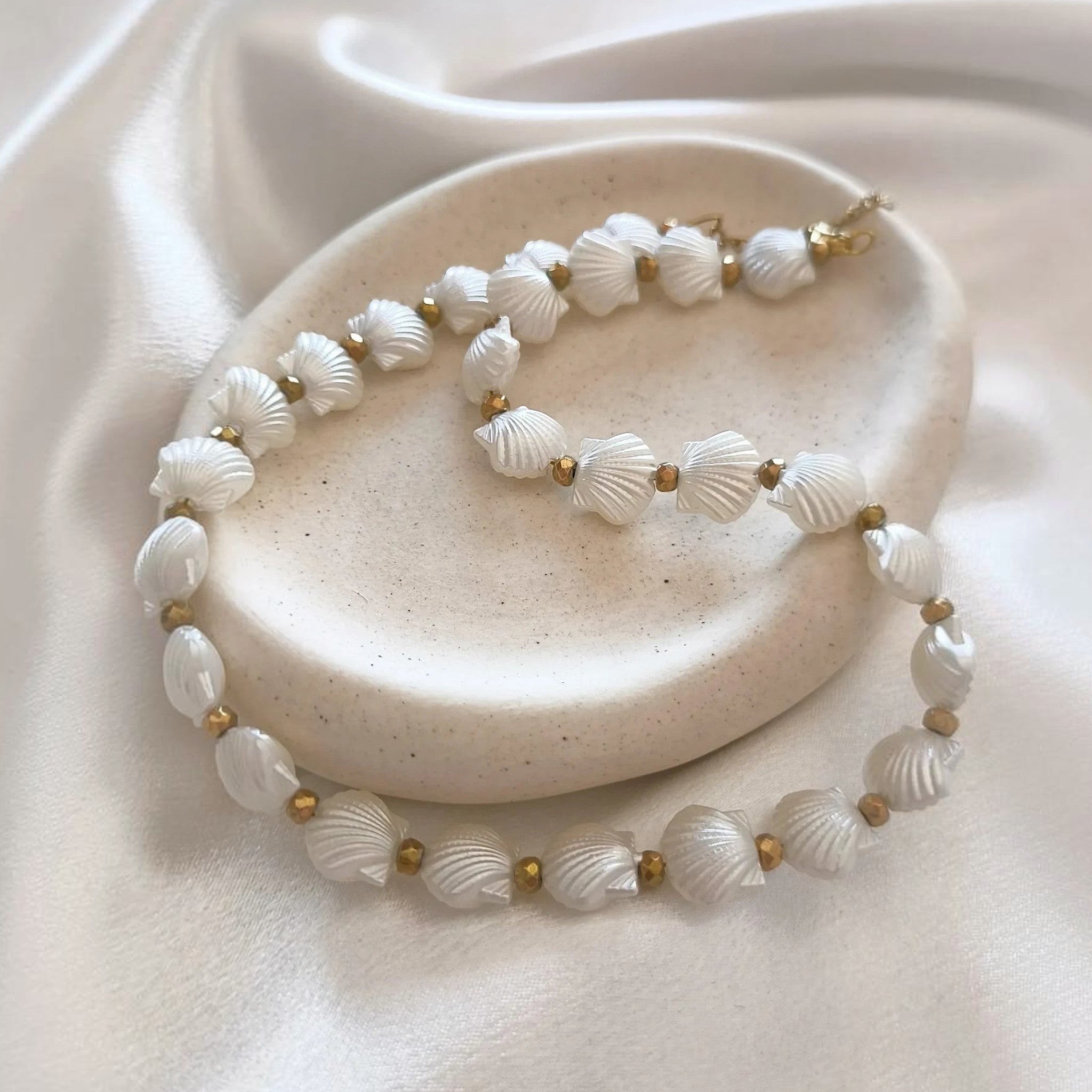 christisaccessories pearlescent white seashell beaded necklace with gold-toned metallic accents on a ceramic dish.