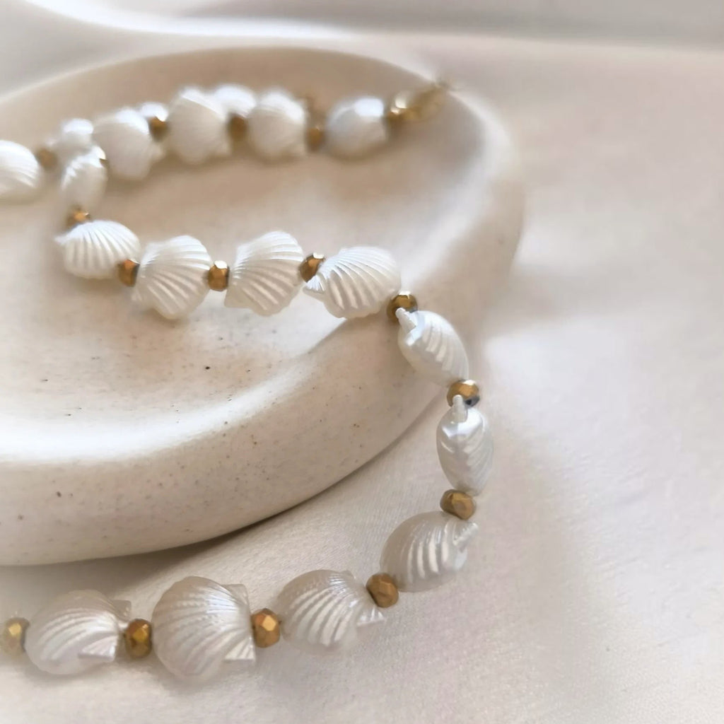 christisaccessories pearlescent white seashell beaded necklace with gold-toned metallic accents on a ceramic dish