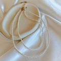 Tiny pearl necklace with rice and round freshwater pearls on white satin fabric