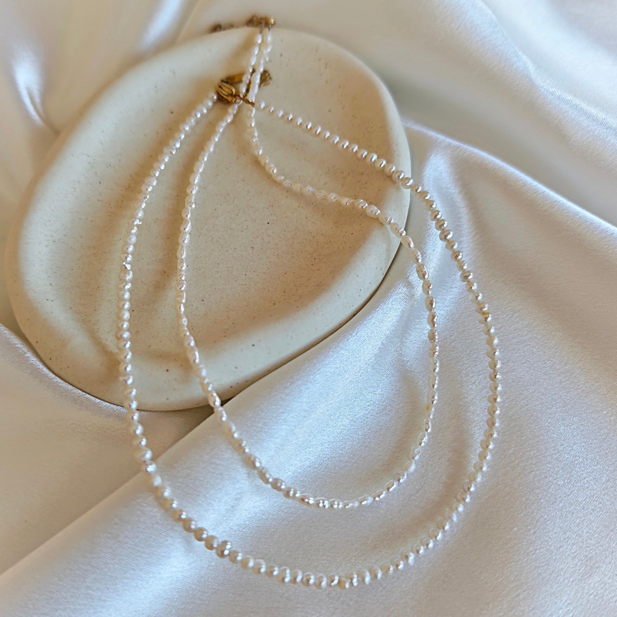 Tiny pearl necklace with rice and round freshwater pearls on white satin fabric