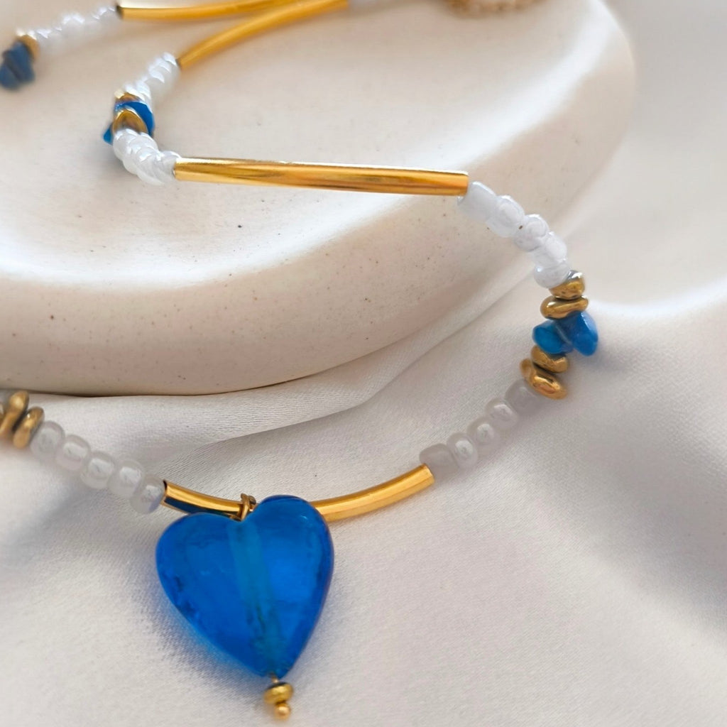 Close up of blue glass heart pendant with gold tube beads