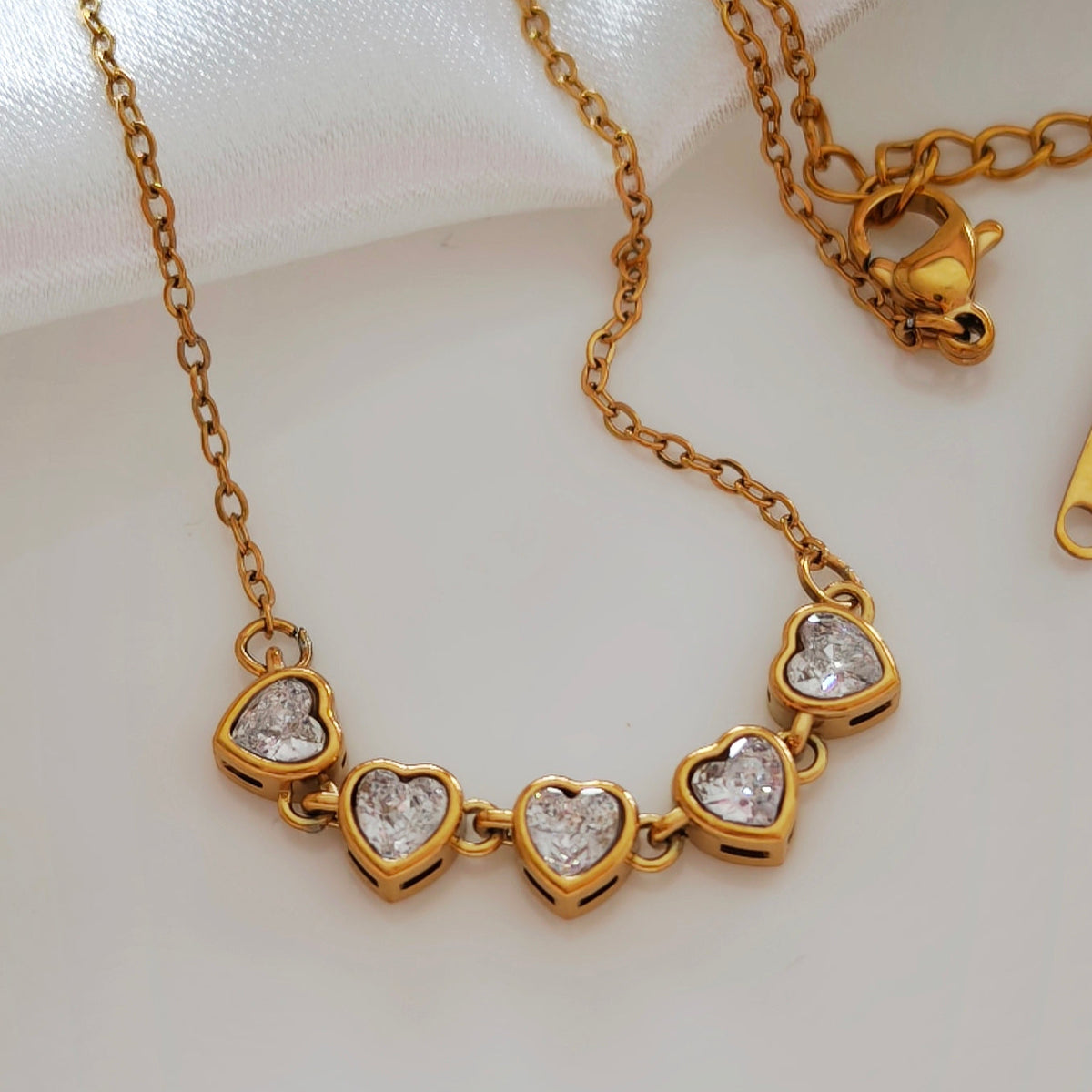 Close-up of five sparkling heart-shaped stones on a gold-tone necklace