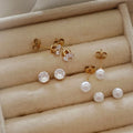Gold stud earrings with white pearl and clear crystal worn on ear