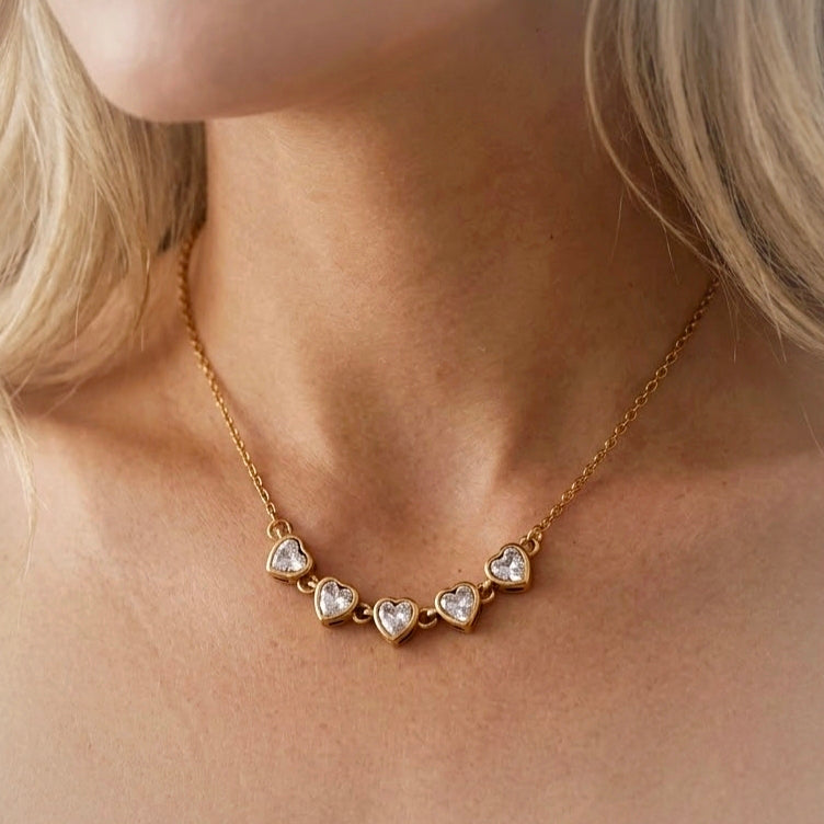 Gold-tone necklace with five sparkling heart-shaped stones worn around the neck