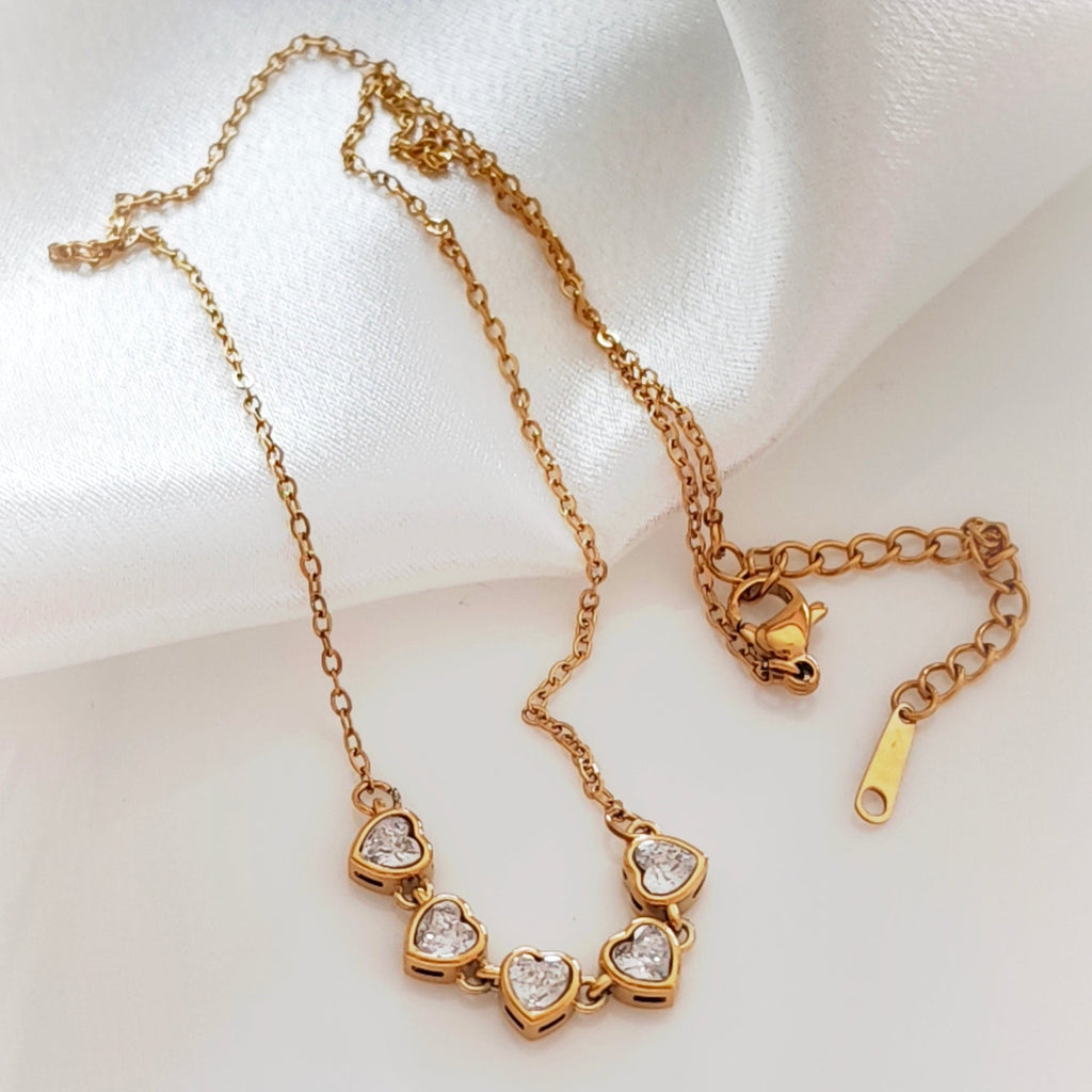Gold-tone necklace with five sparkling heart-shaped stones on a fine chain